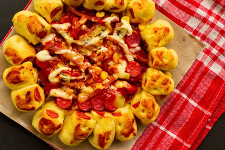A golden-brown baked pastry filled with a vibrant red mixture and topped with melted cheese, presented on parchment paper with a checkered cloth.の写真素材