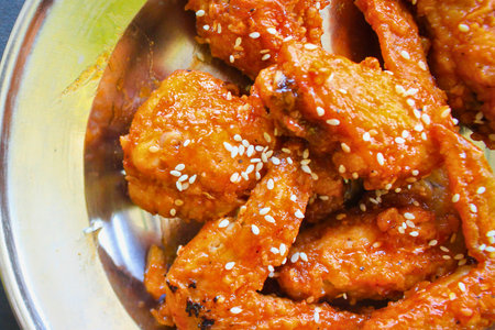 Close-up of crispy, glazed chicken wings coated in a vibrant orange sauce and sprinkled with white sesame seeds.の写真素材