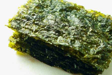 A close-up view of a stack of thin, crispy roasted seaweed sheets, showcasing their textured surface and dark green color.の写真素材