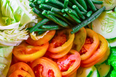 A vibrant close-up of sliced tomatoes, green beans, and lettuce, showcasing a healthy and colorful assortment of fresh vegetables.の写真素材