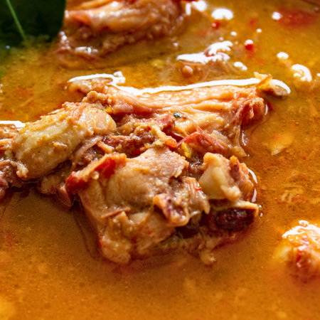 A detailed, appetizing view of tender chicken pieces submerged in a flavorful, golden-orange broth, hinting at a delicious meal.の写真素材