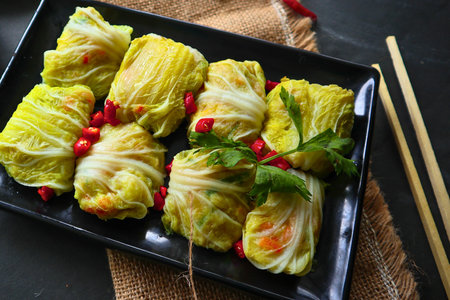 A platter of neatly rolled cabbage leaves, filled with a savory mixture and garnished with red...