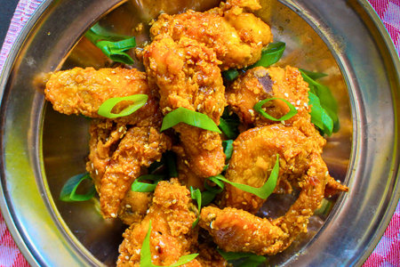 A close-up overhead view of golden brown, crispy fried chicken pieces garnished with fresh green herbs, presented in a shiny metallic dish.の写真素材