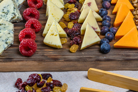 A delicious and colorful assortment of cheeses fruits nuts and grapes arranged on a rustic wooden board.の写真素材