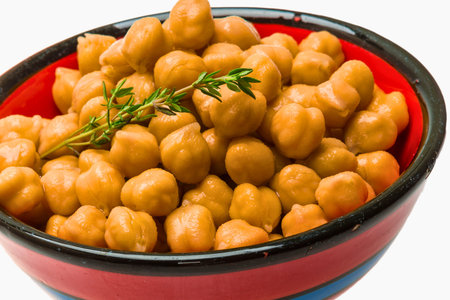 A vibrant red and blue bowl overflowing with cooked chickpeas, topped with a sprig of fresh green thyme.の写真素材
