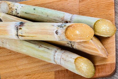 Close-up view of several thick, segmented sugarcane stalks with a natural woody texture, resting on a light brown cutting board.の写真素材