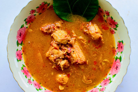 A close-up shot of a delicious chicken curry with tender pieces of chicken in a rich, flavorful sauce, garnished with a fresh green leaf.の写真素材