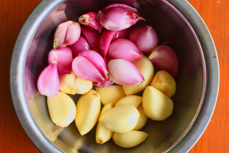 A top-down view of a metal bowl filled with peeled shallots and garlic cloves, ready for cooking.の写真素材