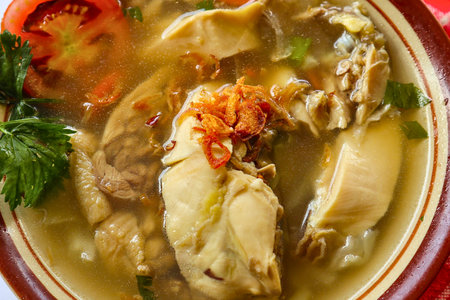 A close-up of a steaming bowl of chicken soup, featuring tender chicken pieces, fresh herbs, and a slice of tomato.の写真素材