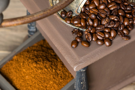 A detailed view of whole roasted coffee beans spilling over a wooden surface next to a pile of ground coffee.の写真素材