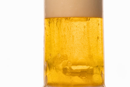A tall glass filled with golden beer, showing effervescent bubbles and a single ice cube, isolated on a white background.の写真素材