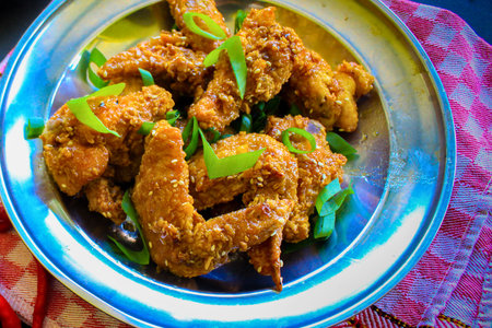 A close-up overhead view of golden brown, crispy fried chicken wings generously seasoned and garnished with fresh green herbs, served in a metal bowl.の写真素材