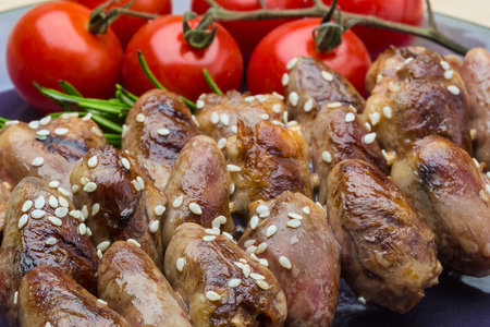 Close-up of grilled chicken hearts seasoned with sesame seeds, served alongside fresh cherry tomatoes on the vine and aromatic rosemary sprigs. A gourmet protein dish.の写真素材