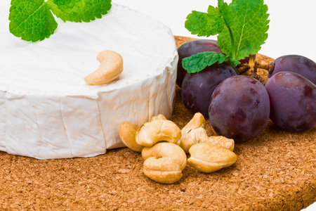A delectable arrangement of creamy camembert cheese, crunchy cashew nuts, juicy red grapes, and fresh mint leaves on a rustic cork board.の写真素材