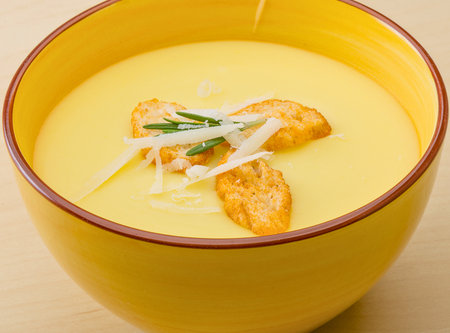 Creamy yellow soup with crispy croutons, savory parmesan cheese, and fragrant rosemary in a yellow bowl. A warm, comforting meal perfect for lunch or dinner.の写真素材