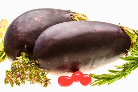 A colorful assortment of fresh garden produce featuring deep purple eggplants, bright red cherry tomatoes, and aromatic green herbs ready for culinary use.の写真素材