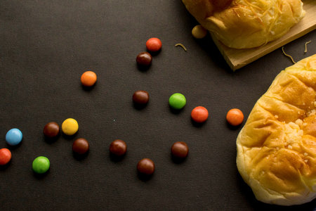 An overhead view featuring an assortment of vibrant, round chocolate candies scattered alongside freshly baked, sweet cheese buns. Perfect for food, snack, or dessert concepts and promotions.の写真素材