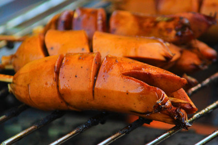 Close-up of golden-brown scored hotdogs sizzling on a hot barbecue grill, ready for a delicious meal. Perfect for summer picnics and casual dining.の写真素材