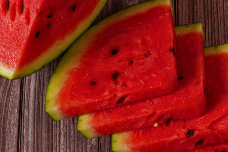 Close-up of vibrant, juicy red watermelon slices with black seeds, neatly arranged on a rustic...