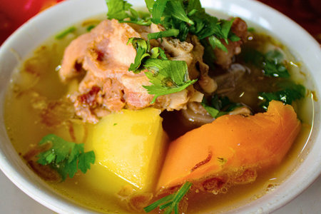 A close-up of a steaming bowl of soup featuring chunks of meat, potatoes, carrots, and fresh green...