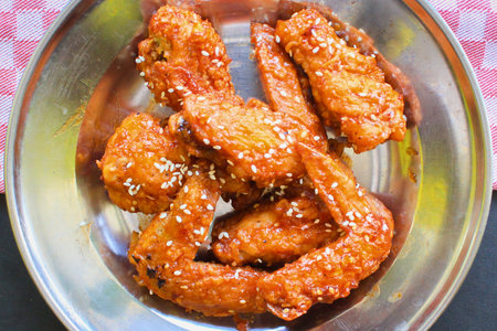 A close-up overhead view of glistening, crispy fried chicken wings coated in a savory sauce and sprinkled with sesame seeds.の写真素材