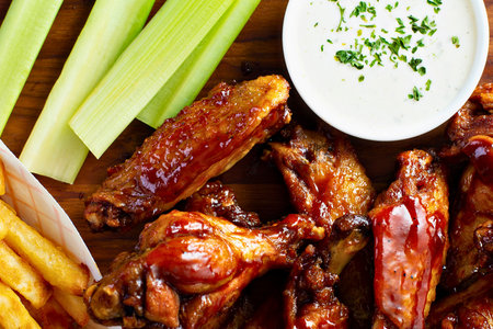 A close up shot of mouthwatering chicken wings served with crispy fries, fresh celery sticks, and a creamy dipping sauce.の写真素材