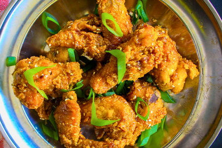 A close-up overhead view of a platter filled with golden brown, crispy fried chicken wings, garnished with bright green scallions.の写真素材