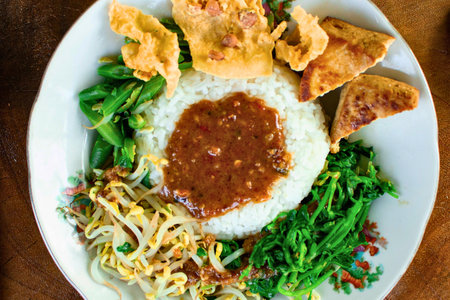 A vibrant plate of Indonesian Nasi Campur featuring fluffy white rice, savory tempeh, and a colorful assortment of fresh vegetables.の写真素材
