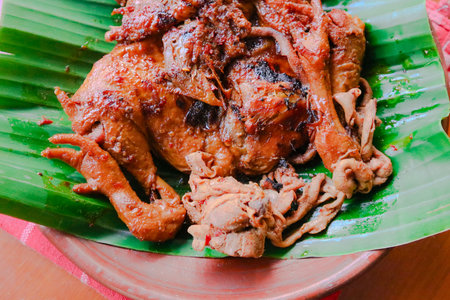 A whole roasted chicken, glistening with sauce, is presented artfully on a vibrant green banana leaf, ready to be enjoyed.の写真素材