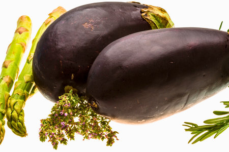 Close-up of two dark purple root vegetables, possibly beets or turnips, alongside fresh asparagus spears and sprigs of herbs.の写真素材