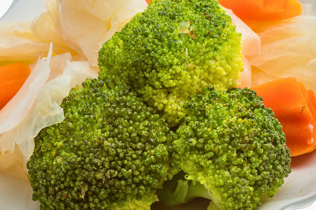 A close-up shot of vibrant steamed broccoli florets and bright orange carrot slices, presented on a white plate.の写真素材