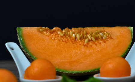 A close-up of a vibrant cantaloupe slice revealing its juicy interior, with perfectly formed melon balls presented in white spoons.の写真素材