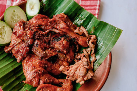 A close-up aerial view of savory grilled chicken pieces arranged on vibrant green banana leaves, garnished with fresh cucumber.の写真素材