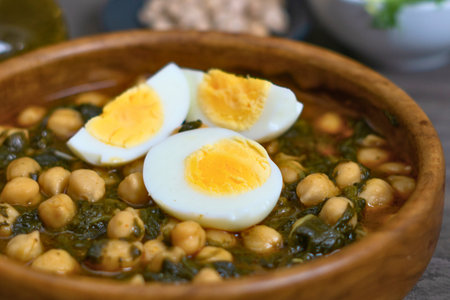 A warm and nutritious chickpea and spinach stew served in a wooden bowl, garnished with sliced hard-boiled eggs.の写真素材