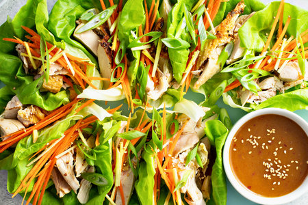 A vibrant platter of crisp lettuce cups filled with shredded vegetables and protein, served with a rich dipping sauce.の写真素材