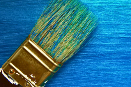 A detailed view of a paintbrush with bristles coated in blue and green paint, poised over a textured blue background.の写真素材