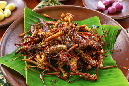 A close-up of a pile of golden brown, crispy fried grasshoppers arranged on a vibrant green banana leaf.の写真素材