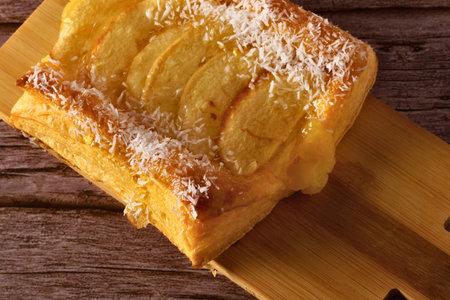 A close-up shot of a golden, flaky puff pastry topped with thinly sliced fruit on a wooden surface.の写真素材