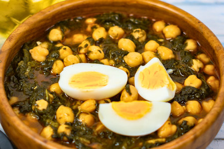 A close-up shot of a rustic wooden bowl filled with a flavorful chickpea and spinach stew, topped with sliced hard-boiled eggs.の写真素材