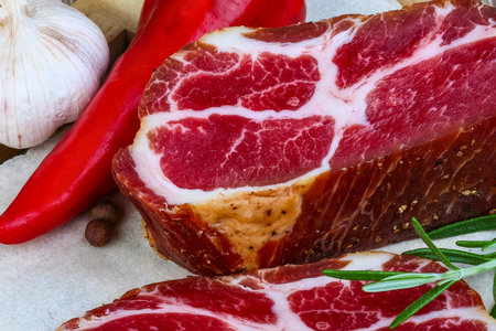 A close-up shot of smoked meat with vibrant red chili peppers, garlic, and fresh rosemary sprigs, suggesting a savory culinary preparation.の写真素材