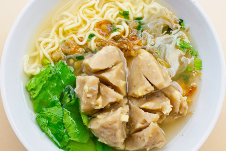 A close-up overhead view of a delicious bowl of Indonesian bakso soup, featuring large meatballs, noodles, and fresh greens in broth.の写真素材