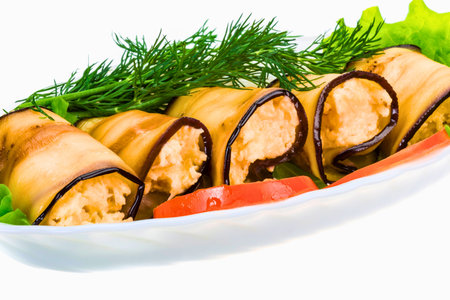 A white platter holds several golden brown eggplant rolls filled with a creamy mixture, garnished with fresh dill and tomato slices.の写真素材
