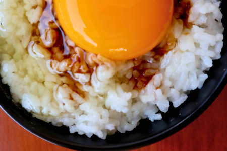 A vibrant raw egg yolk sits atop fluffy white rice, drizzled with a dark sauce, creating a simple yet appetizing dish.の写真素材