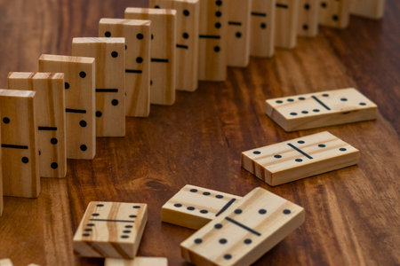 A collection of wooden dominoes, some standing in a curved line and others scattered, resting on a textured wooden table.の写真素材