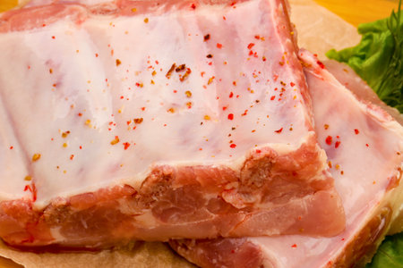 Close-up view of raw pork ribs seasoned with visible spices, prepared for grilling or roasting. A hint of green garnish is visible.の写真素材