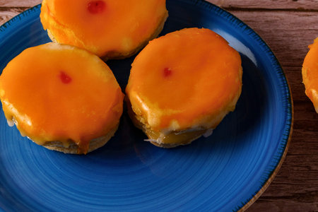 Three golden muffins topped with a vibrant orange glaze, presented on a rustic blue plate.