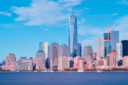 A panoramic view of the New York City skyline, featuring the prominent One World Trade Center, under a bright blue sky.の写真素材