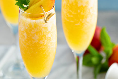 Two tall glasses filled with bubbly, golden peach mimosas, garnished with fresh peach slices and mint. Perfect for brunch or celebration.の写真素材