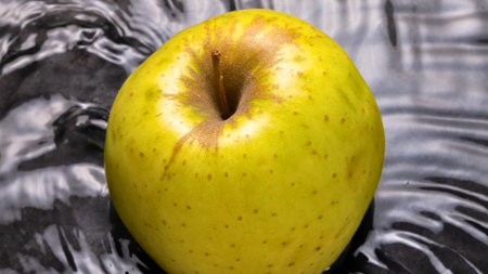 A single, bright yellow apple with visible speckles and a slightly bruised stem area, set against a patterned background.の写真素材