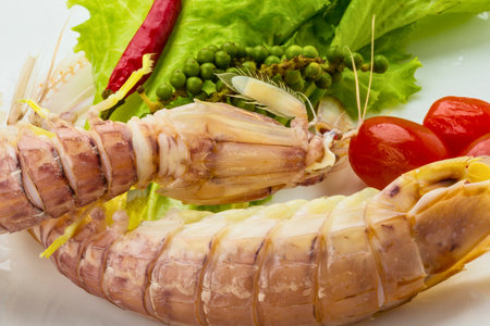 A close-up view of two cooked mantis shrimp served with cherry tomatoes, red chili, green peppercorns, and fresh lettuce.の写真素材